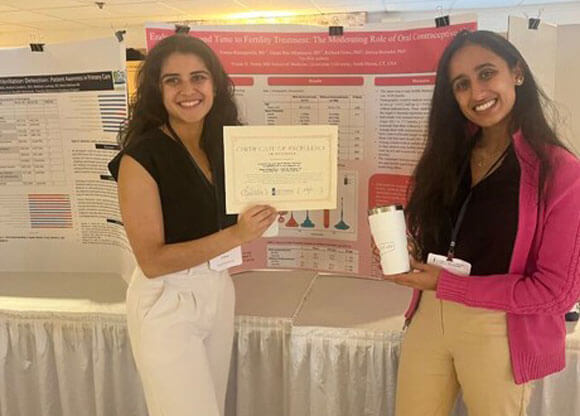 Emma Ratnaparkhi and Ishani Rao smiling with their research poster